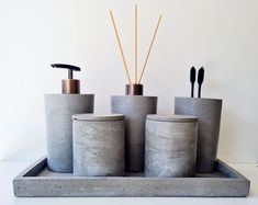 three concrete containers with toothbrushes and soap dispensers on a tray