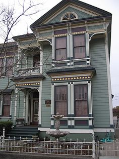 an old victorian house with a fountain in the front yard and fenced in area next to it