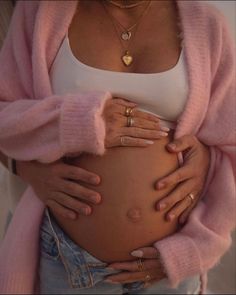 a pregnant woman is holding her stomach with both hands and wearing gold rings on it