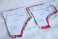 two pieces of paper sitting on top of a white cloth covered tablecloth with red and blue flowers