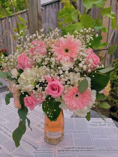 a vase filled with pink and white flowers sitting on top of a table next to a newspaper