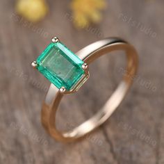 a gold ring with an emerald stone in the center on a wooden table next to yellow flowers