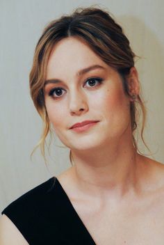 a close up of a person wearing a black dress and posing for a photo in front of a white wall