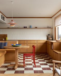 a kitchen with checkered flooring and wooden cabinets, red chair at the table