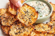 a person dipping some kind of sauce on top of potato chips with black sesame seeds