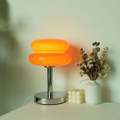 an orange lamp sitting on top of a white table next to a vase with flowers