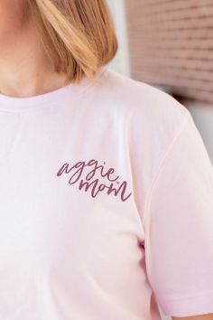 Show your Aggie pride with this stylish Texas A&M Pink Cursive Aggie Mom T-Shirt! It features a light pink shirt with "Aggie Mom" printed in maroon cursive on the left side of the chest. The back has "Aggie Mom" in darker pink with "Texas A&M University College Station" circling it - perfect for any proud Aggie Mom! - Brand: Bella+Canvas - 100% Cotton - Machine Wash Warm/Tumble Dry Low Pink Long Sleeve T-shirt With Text Print, Pink Long Sleeve T-shirt With Letter Print, Pink Long Sleeve T-shirt With Text, Pink Pre-shrunk Long Sleeve T-shirt, Pink Long Sleeve Pre-shrunk T-shirt, Pink Screen Print T-shirt For Mother's Day, Pink Long Sleeve T-shirt With Name Print, Pink Cotton T-shirt With Lettering, Pink Casual Top With Name Print