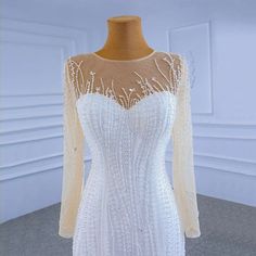 a white wedding dress with sheer sleeves and beadings on the neckline, in front of a mannequin