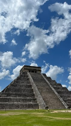 an ancient pyramid in the middle of a green field under a blue sky with clouds