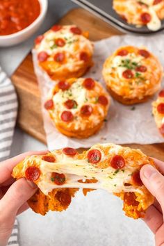 a person holding up a piece of pizza in front of some muffins with pepperoni on them