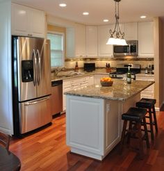 a large kitchen with stainless steel appliances and white cabinets is pictured in this image, the island has two stools on it