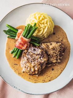 a white plate topped with meat covered in gravy and green asparagus