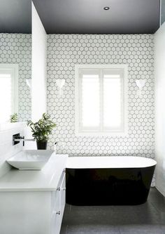 a black and white bathroom with a bathtub, sink, mirror and plant in it