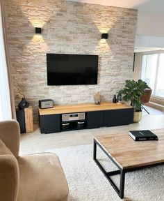 a living room with couches, tables and a television on a brick wall behind it