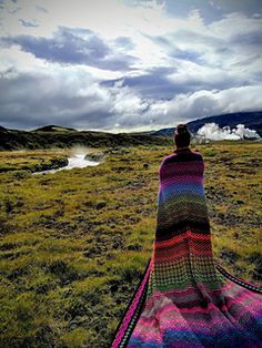 a woman sitting on top of a blanket in the middle of a grass covered field