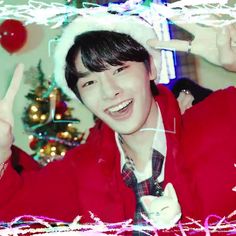 a young man wearing a santa hat and giving the peace sign with his hand while standing in front of a christmas tree