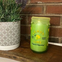 a green jar sitting on top of a wooden table next to a potted plant