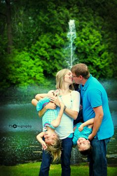 a family poses for a photo in front of a fountain with their two children on their shoulders