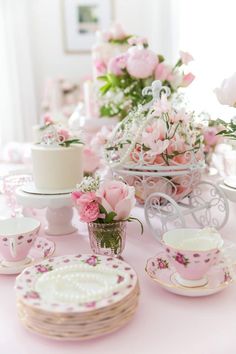 a table topped with pink and white cake next to cups and saucers filled with flowers