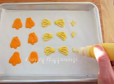 someone is decorating some cookies with orange icing on a sheet of baking paper