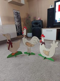 three wooden chickens standing on top of a green leafy plant in front of a tv