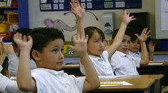 several children sitting at desks with their hands in the air