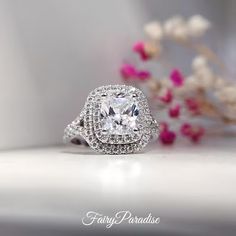 a cushion cut diamond surrounded by halos and pave diamonds on a white surface