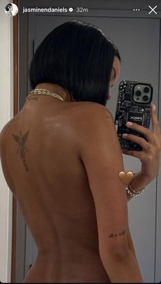 a woman taking a selfie in front of a mirror with tattoos on her back