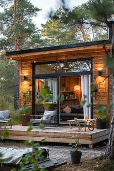 a small wooden cabin in the woods with patio furniture and lights on it's side