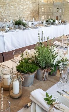 the table is set with white flowers and greenery in buckets on top of it