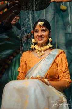 a woman in yellow and white sari is being sprayed with water from a shower