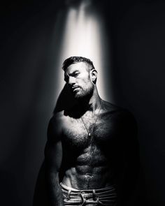 a man with no shirt standing in front of a light that is shining on him