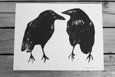 two black birds standing next to each other on top of a wooden table with wood planks