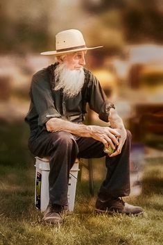 an old man with a long white beard sitting on a chair in the grass wearing a hat