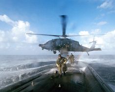 two men are standing on the deck of a ship as a helicopter flies over them