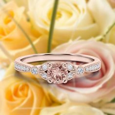 a pink diamond ring sitting on top of a bouquet of flowers next to white roses