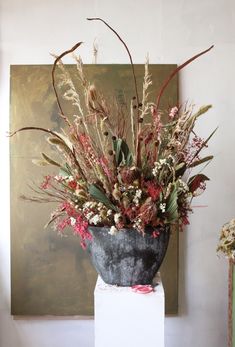 a vase filled with lots of flowers sitting on top of a white pedestal next to a painting