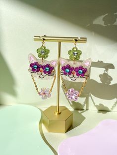 a pair of pink and green cat earrings on a stand