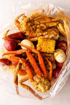 crab legs, potatoes and corn on the cob in a plastic bag with white background