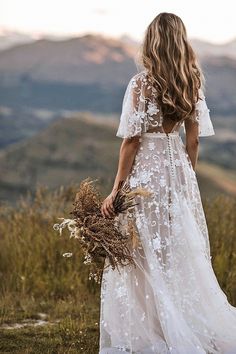 a woman in a white dress is standing on a hill with her back to the camera