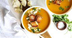 two bowls filled with soup next to cauliflower