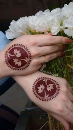 two hands with henna tattoos on their palms and flowers in the vase behind them