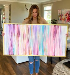 a woman holding up a large painting in her living room