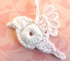 a white crocheted angel ornament hanging from a string on a pink background