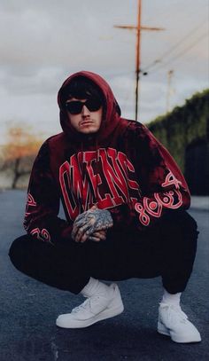 a man in a red hoodie squatting on the ground with his hands crossed