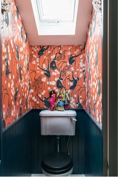 a small bathroom with an orange floral wallpaper and white toilet in the corner under a skylight