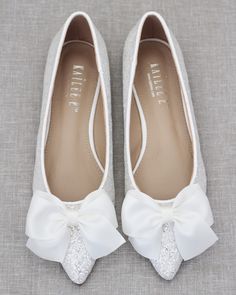 a pair of white shoes with a bow on the front and bottom, sitting on a gray surface