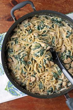 a skillet filled with pasta and spinach covered in sauce on top of a wooden table