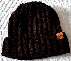 a brown knitted beanie hat with a tag on the front sitting on top of a bed