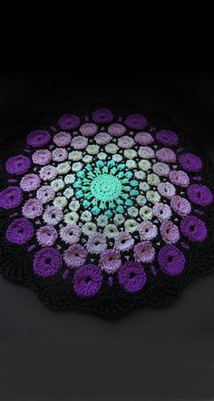 a crocheted doily with pink and purple flowers on it, in the dark